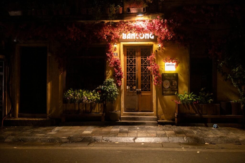 Entrée privée discrète la nuit dans une ville tropicale, éclairage chaleureux et plantes en pot.