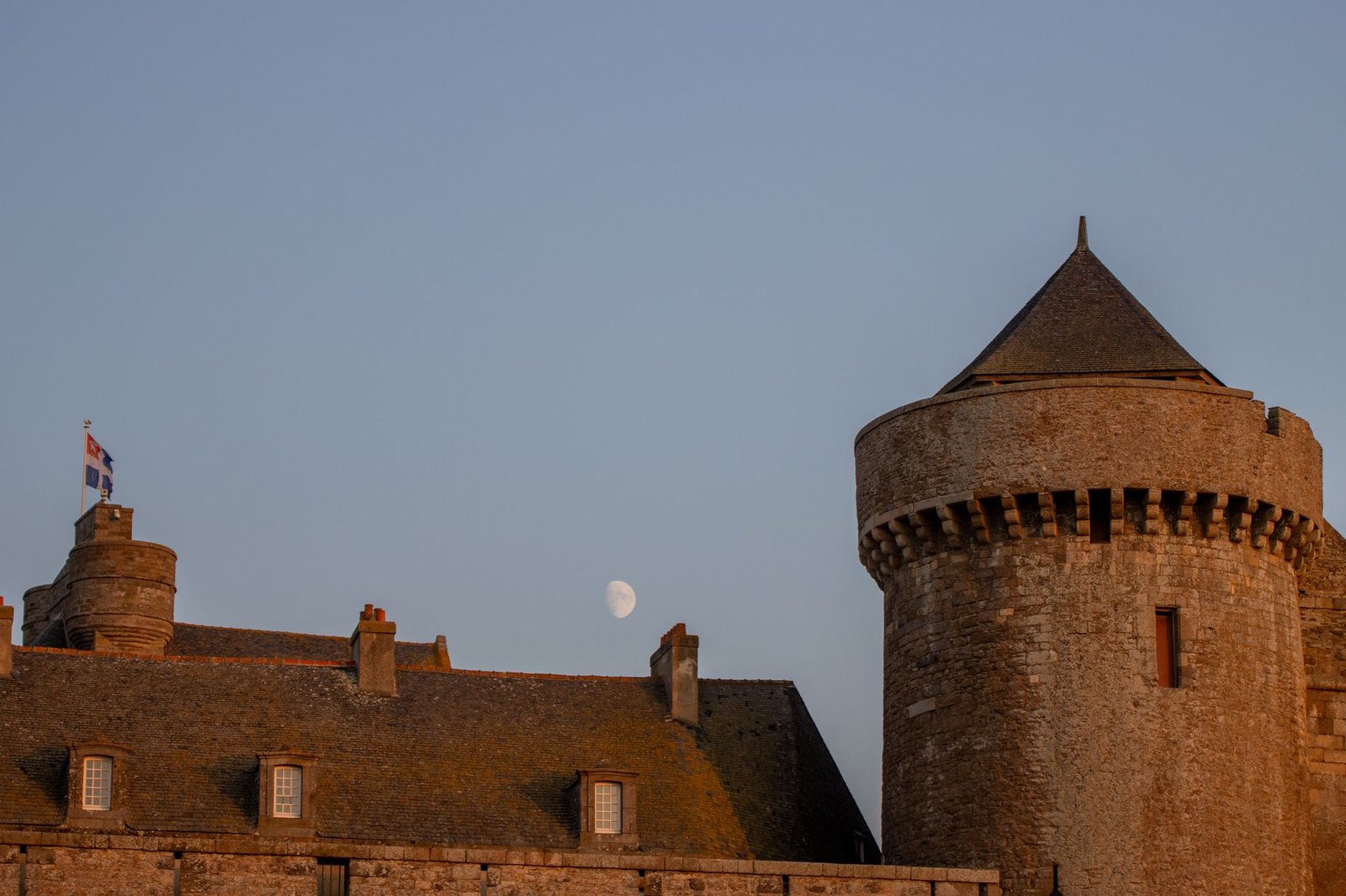 Ruelle pavée de Saint-Malo au crépuscule avec lumières chaudes et remparts en arrière-plan
